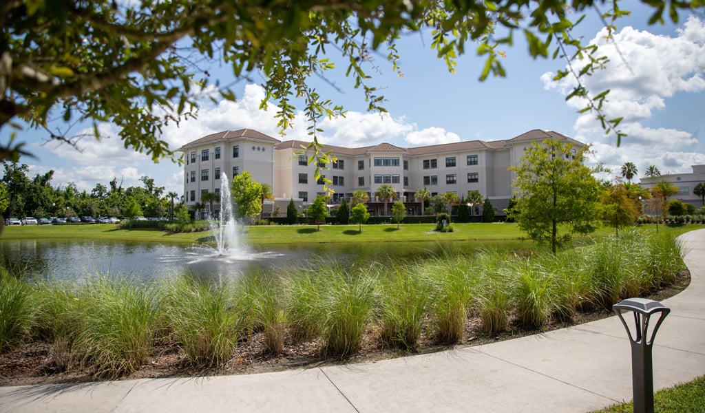 Mayflower campus featuring walkways and a pond with fountain in front of a 4-story residence. 