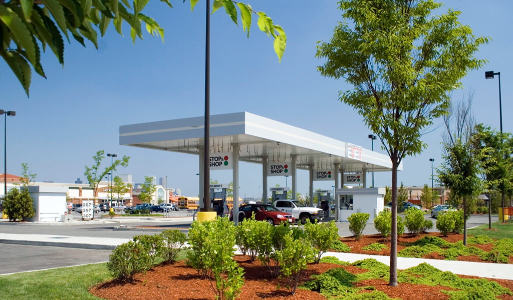 Stop and Shop fueling station in front of a shopping center with a red car and light gray truck at the pump stations. 