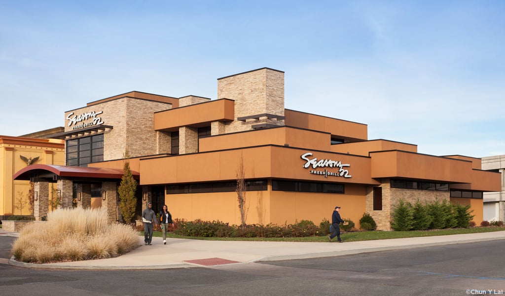 Modern Seasons 52 restaurant exterior with stone and orange facade, people walking outside