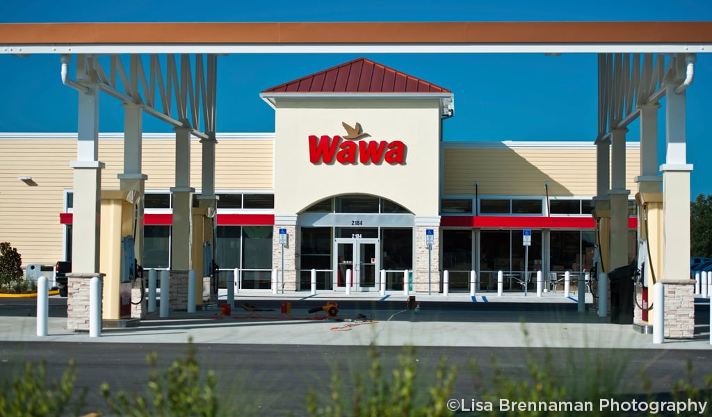 Front view of a Wawa store with gas pumps in the foreground under a clear blue sky.