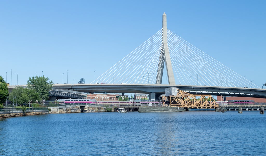 A train crossing a drawbridge, beneath a suspension bridge.