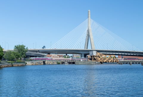 A train crossing a drawbridge, beneath a suspension bridge.