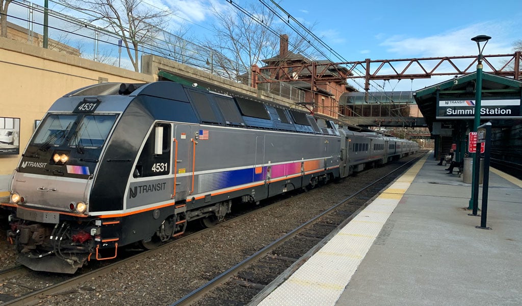 A NJ TRANSIT train with a blue, pink, and orange gradient stripe sits at Summit Station. 