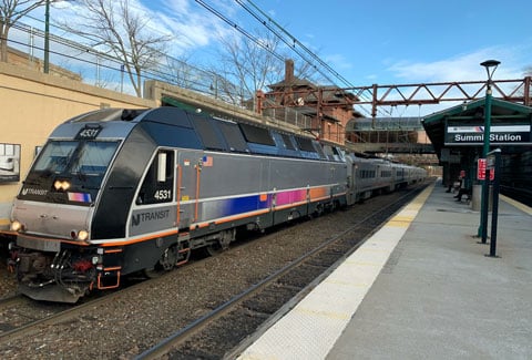 A NJ TRANSIT train with a blue, pink, and orange gradient stripe sits at Summit Station. 