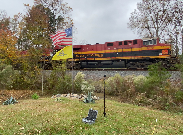 Noise monitoring of an engine on train tracks passing by an American flag.