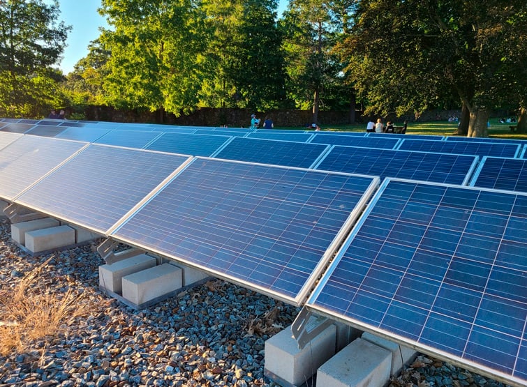 Ground-mounted solar array near park with people sitting in the distant background.