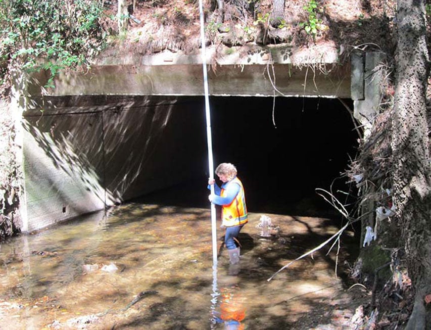 Woman standing in river under a bridge conducting analysis.