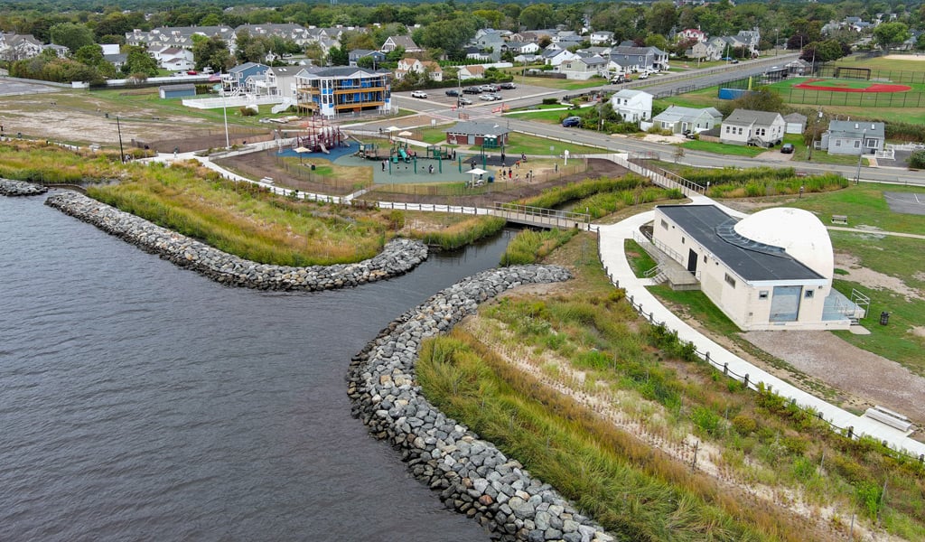 Aerial view of Shorefront Park, showing open green spaces, walking paths, shoreline features, playground, and surrounding natural landscape.