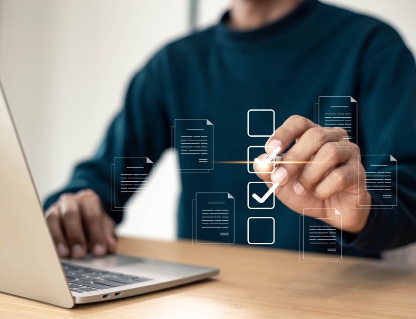 A person in a dark shirt uses a laptop, selecting virtual checkboxes on a digital interface with document icons hovering above.