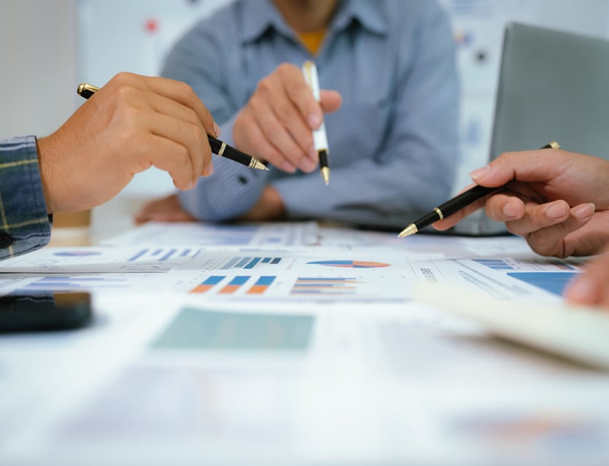 Three people at a table discussing graphs and charts with pens.
