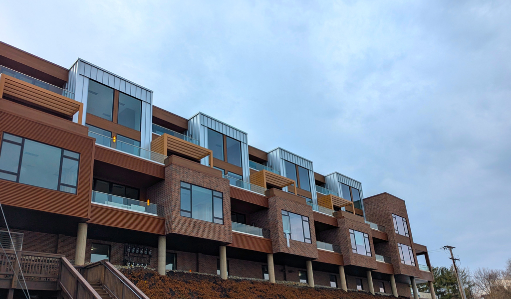 Modern multi-story apartment building on sloped lot with large windows & balconies. 