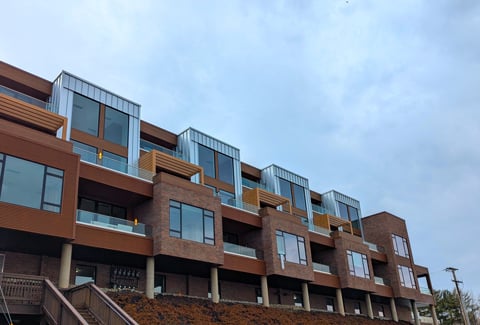 Modern multi-story apartment building on sloped lot with large windows & balconies. 