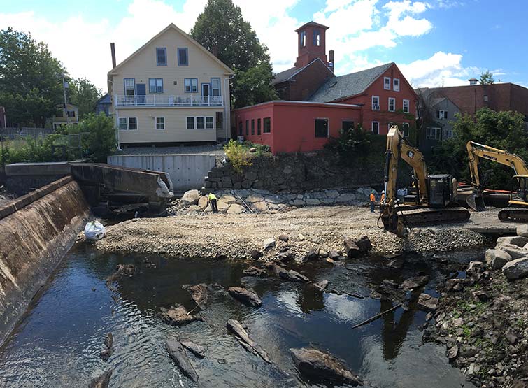 Dry section of rocky river bed with constructinon vehicles removing old dam 