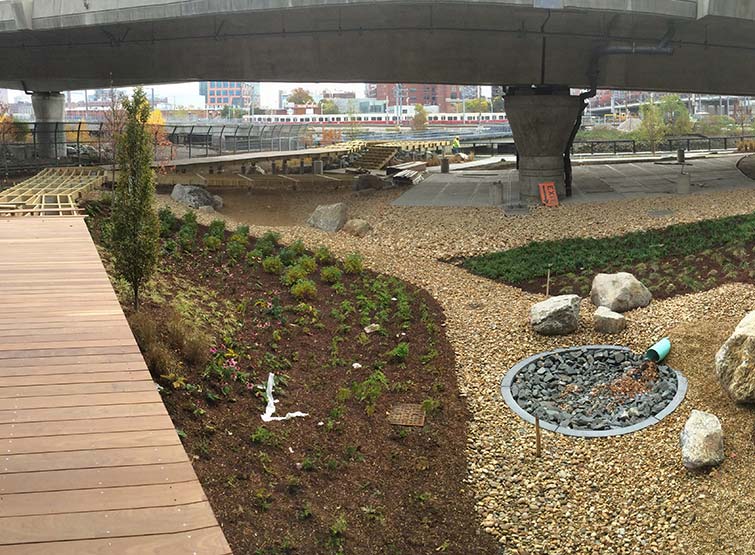 Highway overpass with walkways, greenery and rocks underneath 