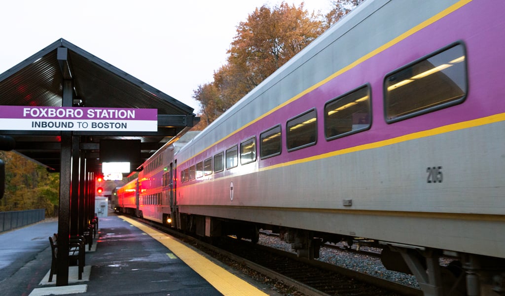 An MBTA Commuter Rail train pulling into Foxboro Station with a red wayside signal in the background.