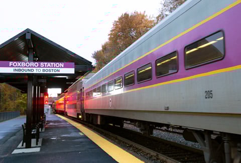 An MBTA Commuter Rail train pulling into Foxboro Station with a red wayside signal in the background.