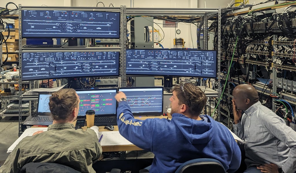 Three men look at signal systems on a computer at factory acceptance testing.