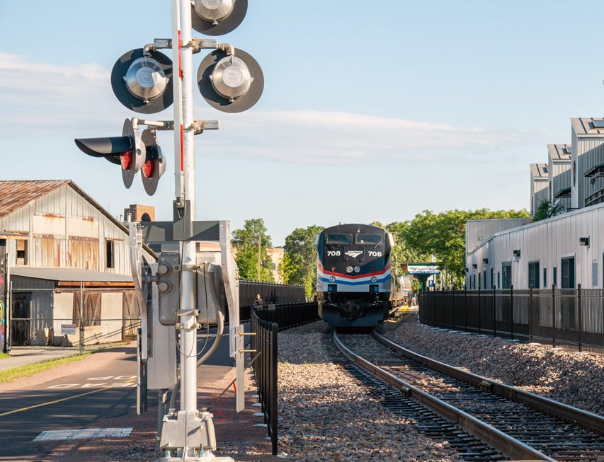 An Amtrak train on tracks with a railroad crossing warning system in the foreground
