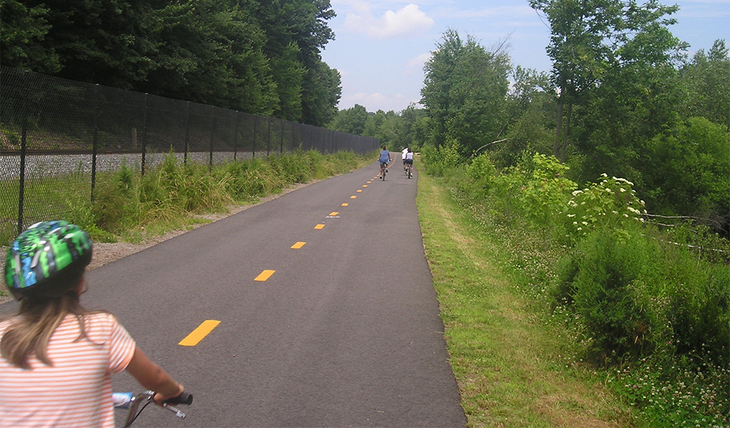People ride bicycles along a trail next to railroad tracks.
