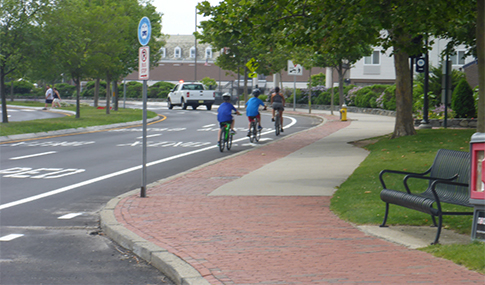 People ride bicycles single file in a designated bike lane in a roadway.