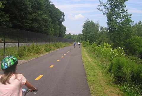 People ride bicycles along a trail next to railroad tracks.