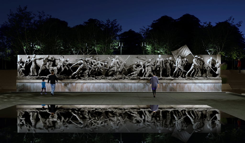 Long bronze wall sculpture of people in front of reflecting pool at night