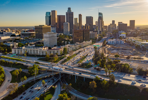 Aerial view of LA skyline with skyscrapers and freeway traffic below.