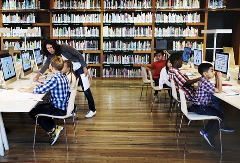 Children sitting at desks working on computers in a library.