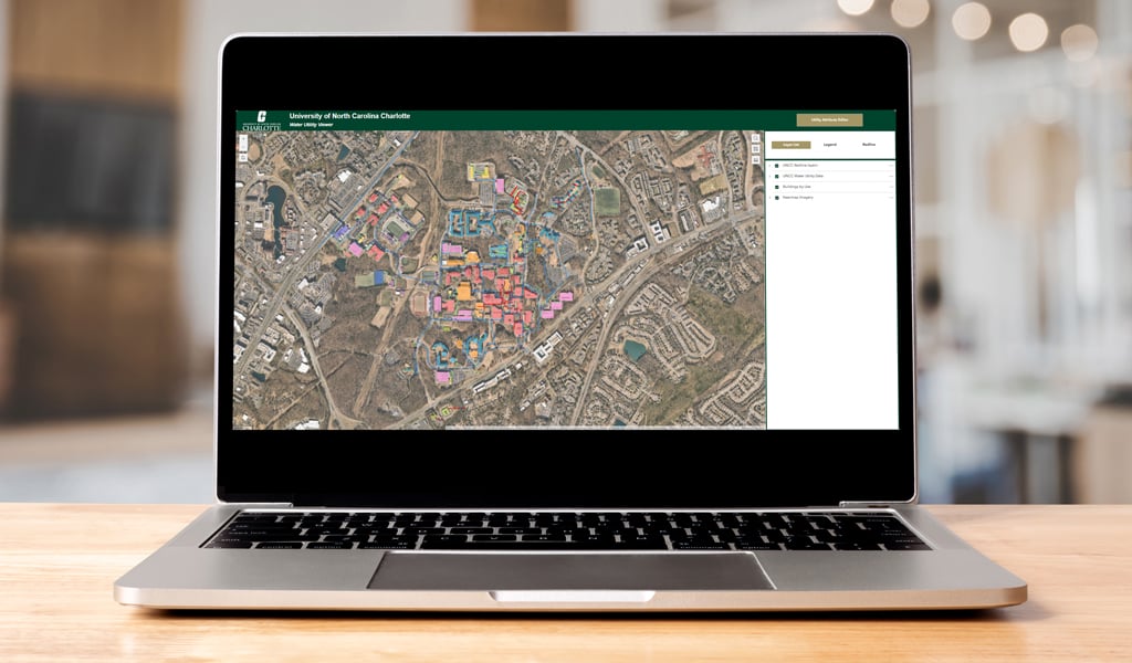 Laptop screen with a UNC Charlotte dashboard displaying an aerial view of campus and highlighted buildings.