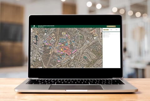 Laptop screen with a UNC Charlotte dashboard displaying an aerial view of campus and highlighted buildings.
