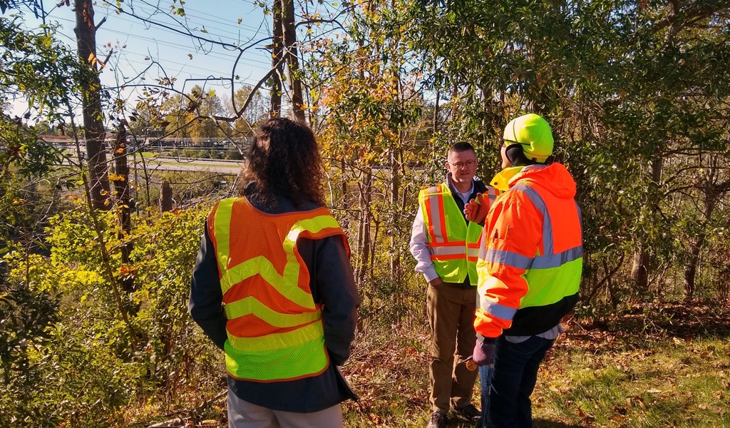 Three VHB staff wearing safety vests gather during a site visit. 