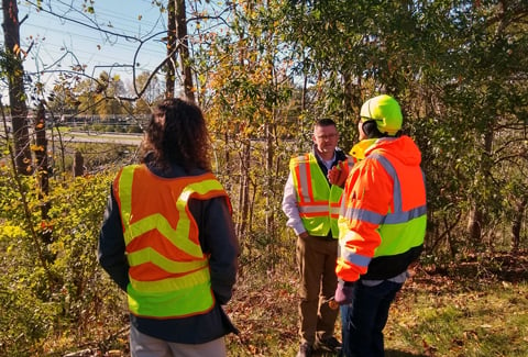 Three VHB staff wearing safety vests gather during a site visit. 