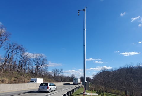 Traffic camera mounted on a tall pole along I-70 in Pennsylvania, with cars and trucks traveling on the highway.