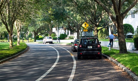 A pedestrian walks on a subdivision sidewalk near a pedestrian crossing sign.