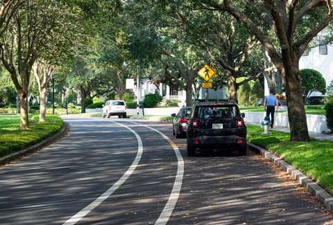 A pedestrian walks on a subdivision sidewalk near a pedestrian crossing sign.