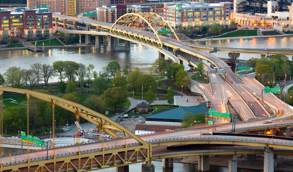 Aerial view of bridges crossing the Monongahela and Allegheny Rivers in Pittsburgh, PA, with the downtown skyline visible.