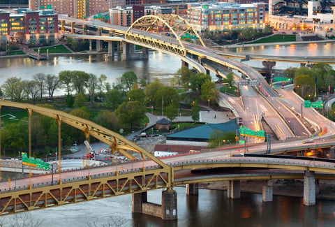 Aerial view of bridges crossing the Monongahela and Allegheny Rivers in Pittsburgh, PA, with the downtown skyline visible.