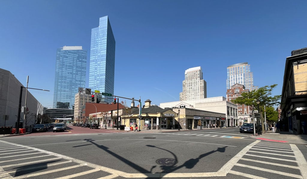Street intersection featuring crosswalks, traffic lights, and a mix of modern skyscrapers and older low-rise buildings under a clear blue sky. 
