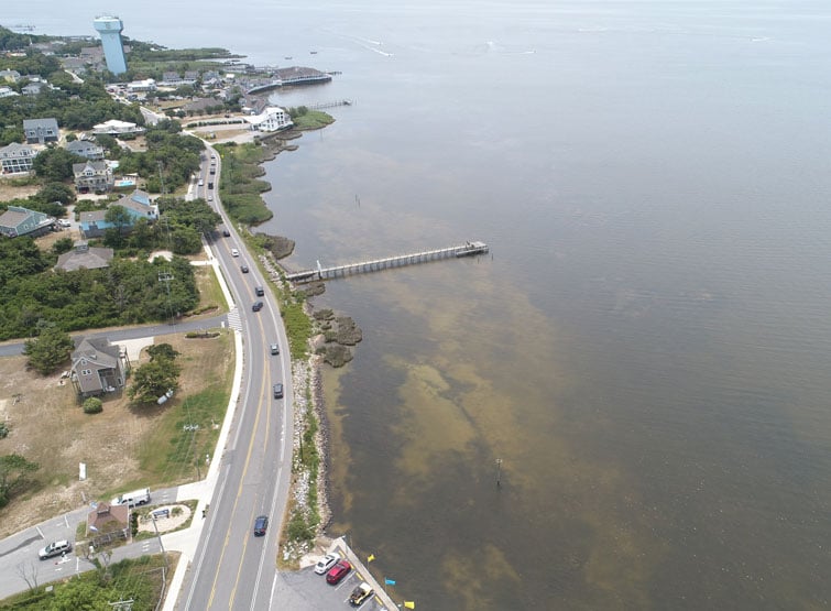 Aerial view of a coastal road next to a body of water, with a pier extending into the water.