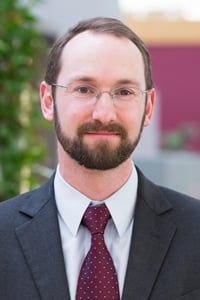 A person in a suit and tie is standing with an office background.