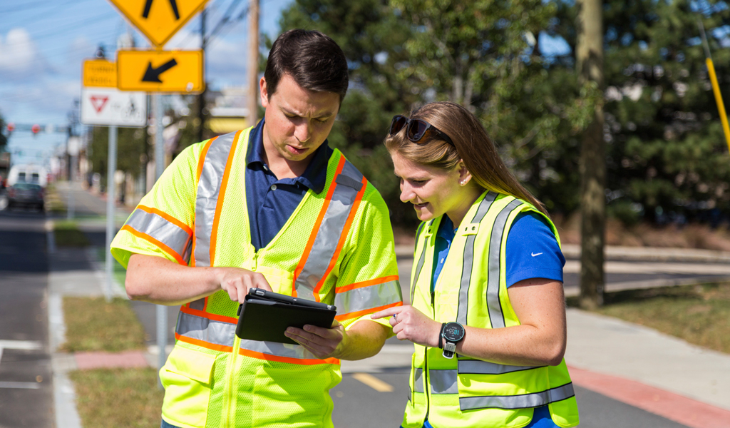 Two VHB team members wear safety vests and work together in the field