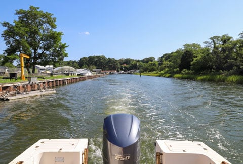 A view from a boat moving down a sunny channel lined with small docks, structures and trees.