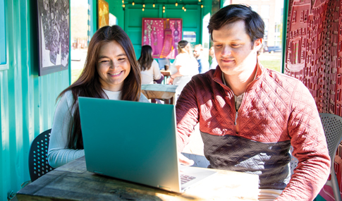 A man and a woman smiling looking at a laptop.