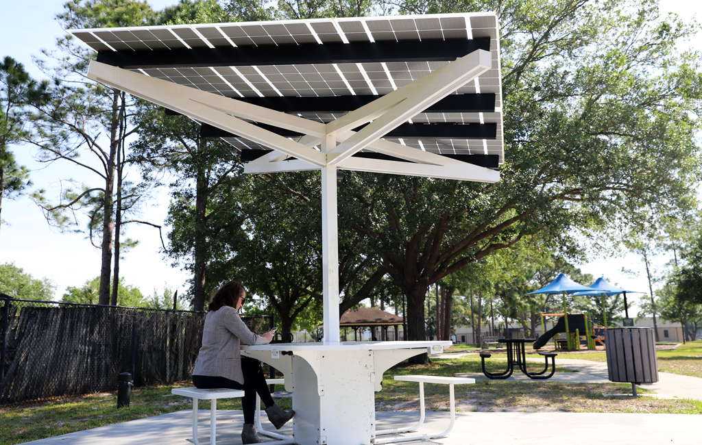 A woman sits at a table with solar panels in a park.