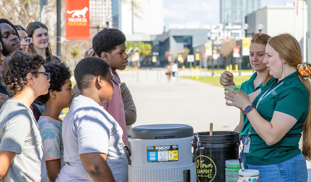A group of middle school children being educated about the REACH mobile hub in Orlando outdoors on a sunny day.