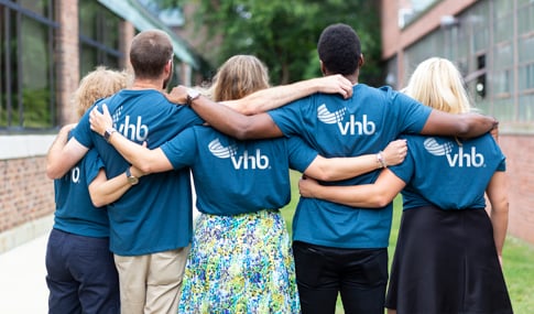 Five people wearing blue VHB tee shirts stand with their arms around each other.