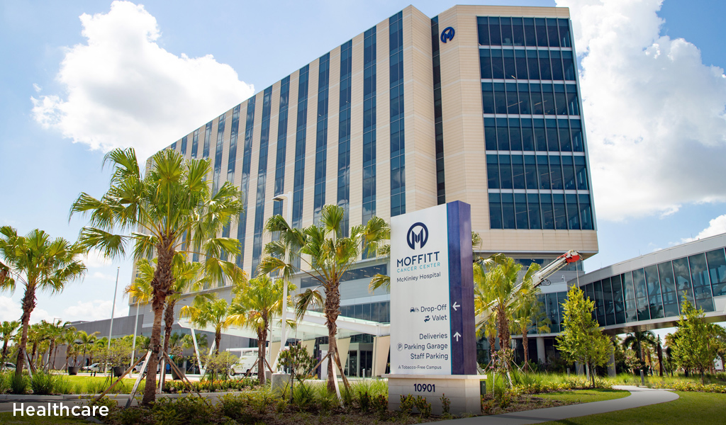 A multi-story new hospital with tropical trees at the entrance