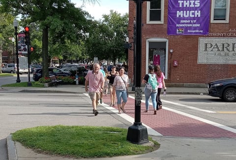 Pedestrians crossing a street in downtown Keene, NH near a signpost and Parrish Shoes wall mural.