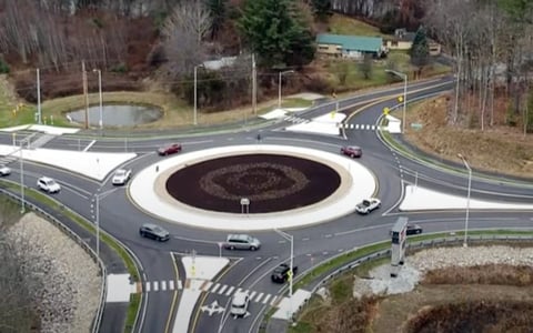 Roadway Design- Aerial view of a traffic roundabout with multiple exits and vehicles. The roundabout features a decorative center with landscaping.