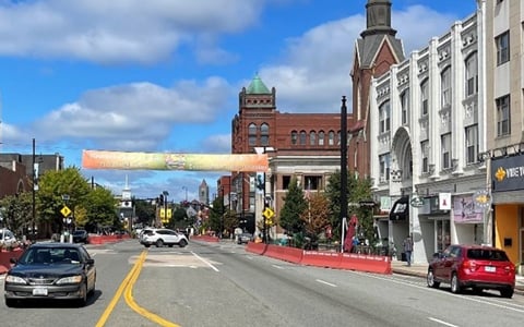 Traffic/Safety Studies- View of Main Street in Nashua, NH with a banner reading "Welcome" across the road, flanked by historic buildings under a partly cloudy sky.